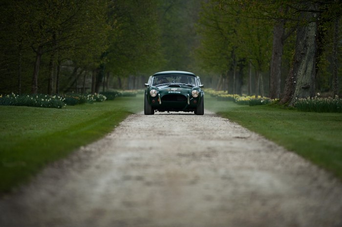 Green vintage car driving on a dirt road lined with trees