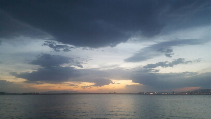 Sunset over the sea with city lights on the horizon