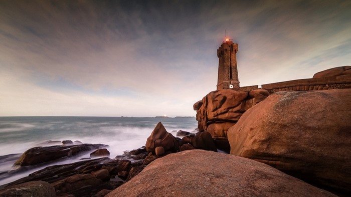 Lighthouse on rocky coast at sunset