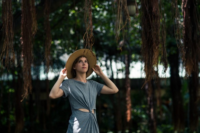 Woman in sun hat looking up under hanging vines