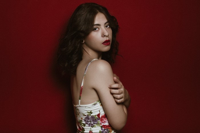 Woman with dark wavy hair and floral camisole against red background