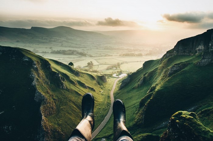 Person sitting on a cliff overlooking a valley at sunset