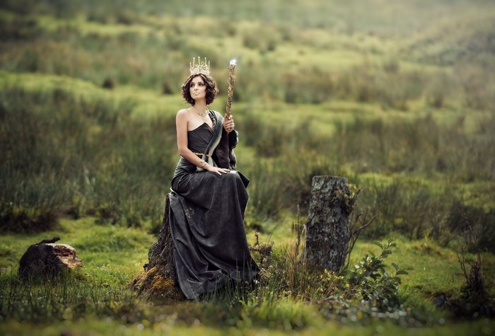 Woman in a dark gown and crown holding a staff
