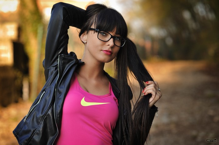 Woman with glasses and pigtails wearing a pink tank top and leather jacket