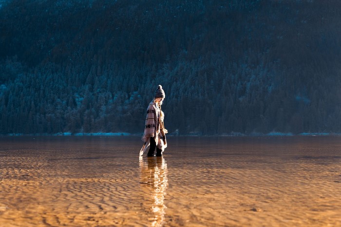 Woman in poncho standing in shallow water with forest background