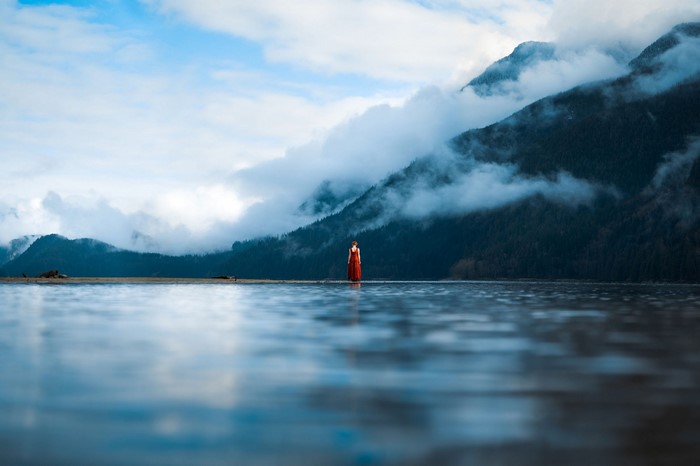 Woman in red dress by misty mountains and lake