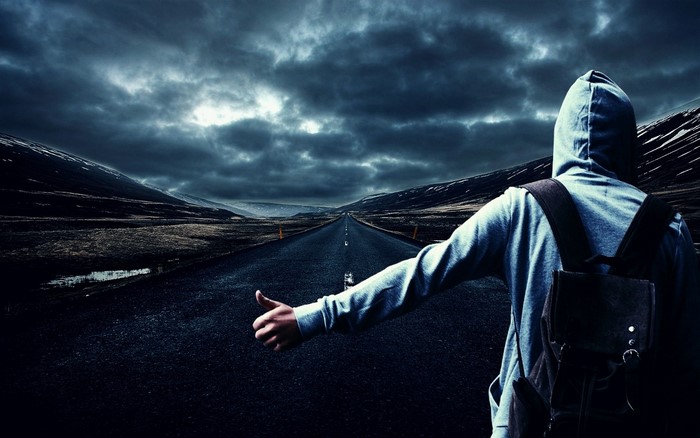 Person hitchhiking on a desolate road under stormy skies
