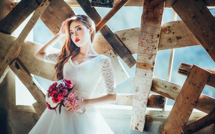 Bride in white lace dress holding flowers with wooden background