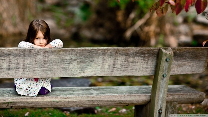 Little girl on a wooden bench in nature