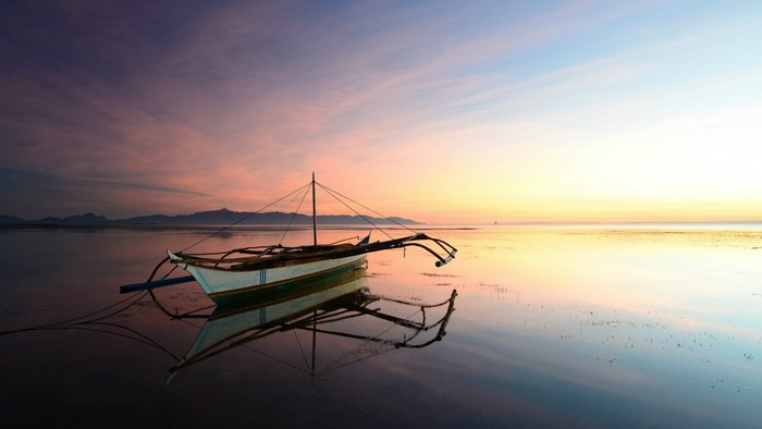 Boat on calm sea at sunset with mountain silhouette