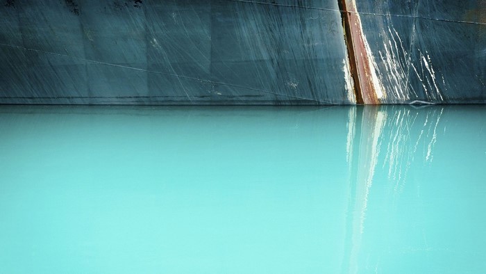 Dark hull of a ship reflected in turquoise water