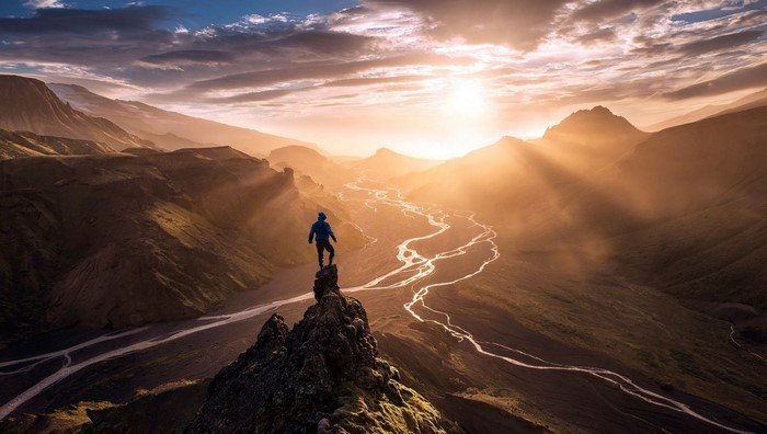 Man on cliff overlooking river valley at sunset