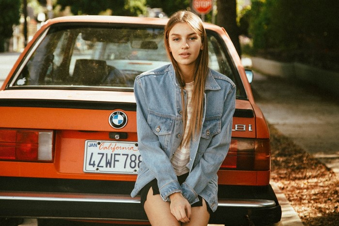 Woman in denim jacket leaning on orange BMW E30