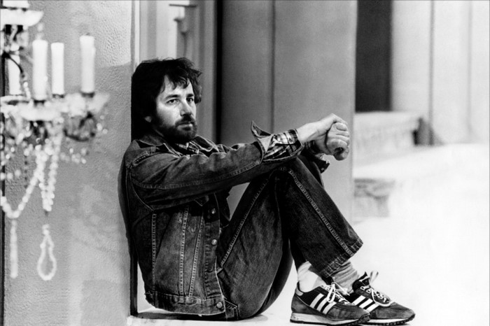 Steven Spielberg sitting in a jean jacket and Adidas sneakers