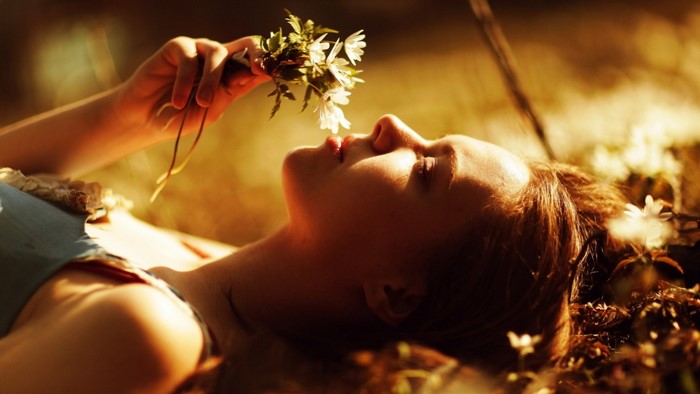 Woman lying down smelling flowers in sunlight