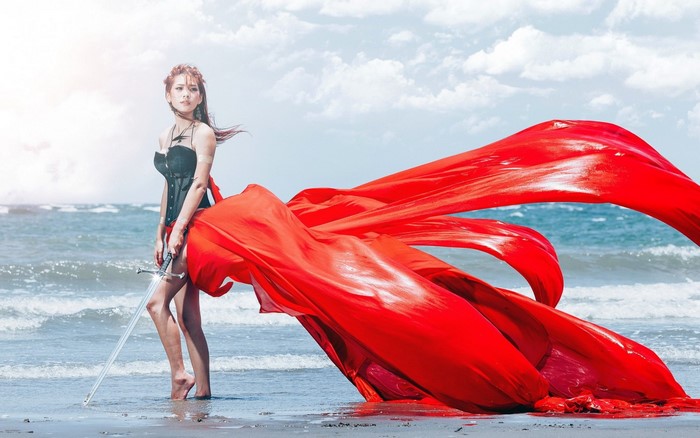Asian woman with sword and red fabric on beach