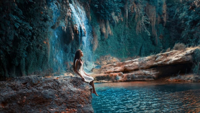 Woman sitting on a rock by a waterfall