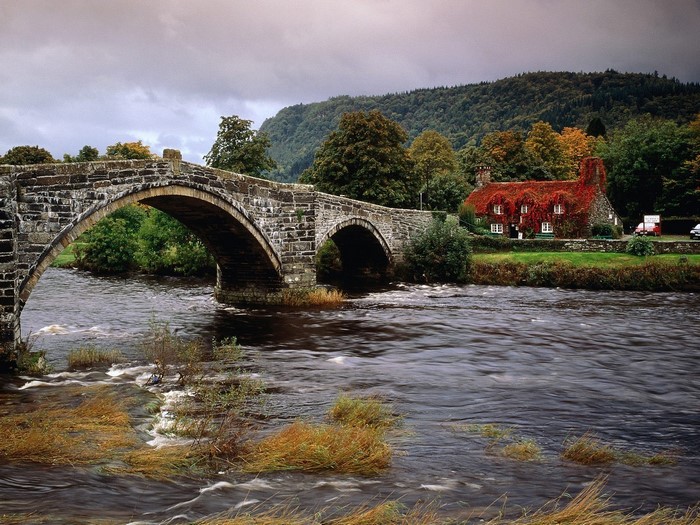 Stone bridge over a river with a red-roofed house