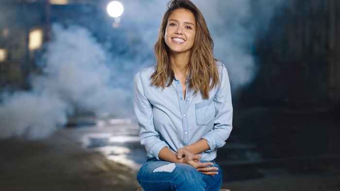 Jessica Alba sitting in a denim shirt and ripped jeans