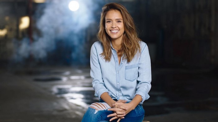 Jessica Alba sitting in a denim shirt and ripped jeans