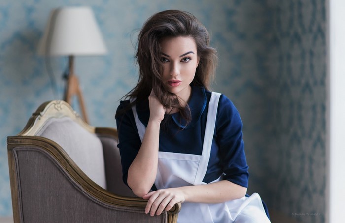 Woman in blue dress and white apron sitting on a couch