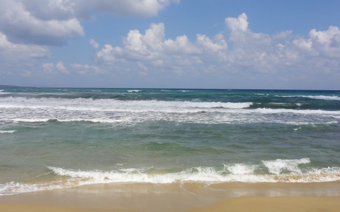 Ocean waves crashing on a sandy beach under a cloudy sky
