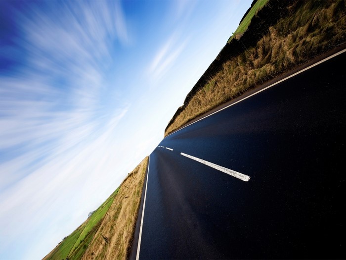 Road through a grassy landscape under a cloudy sky