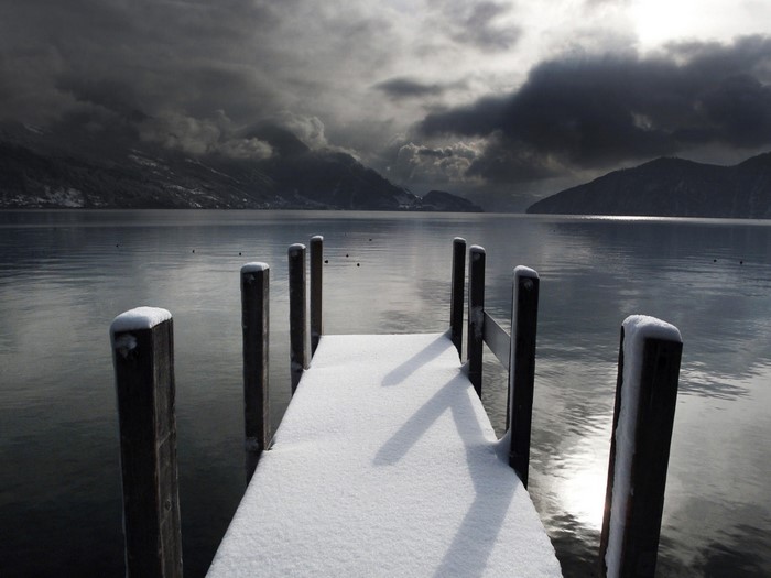 Snow-covered pier on a lake with mountains and stormy clouds