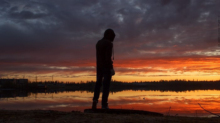 Person in hoodie by lake at sunset