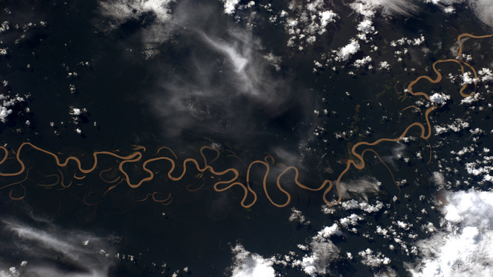 Aerial view of a winding river through a dark forest with clouds