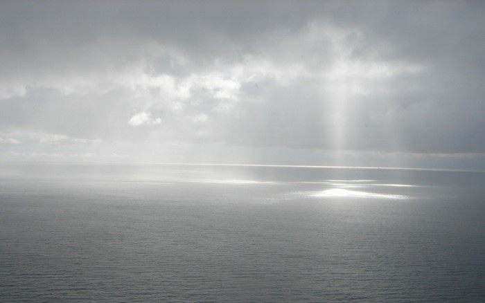 Sunlight beams through clouds onto the ocean horizon