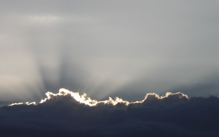 Sunlight beams through dark clouds at the horizon