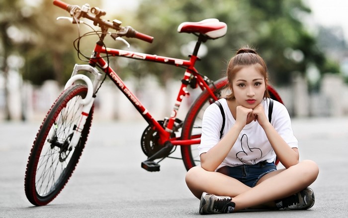 Young woman sitting by a red bicycle