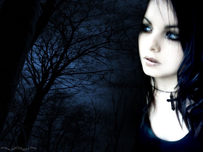 Gothic woman with blue eyes and cross necklace in dark forest