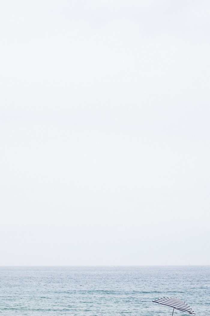 Minimalist beach scene with striped umbrella and ocean horizon