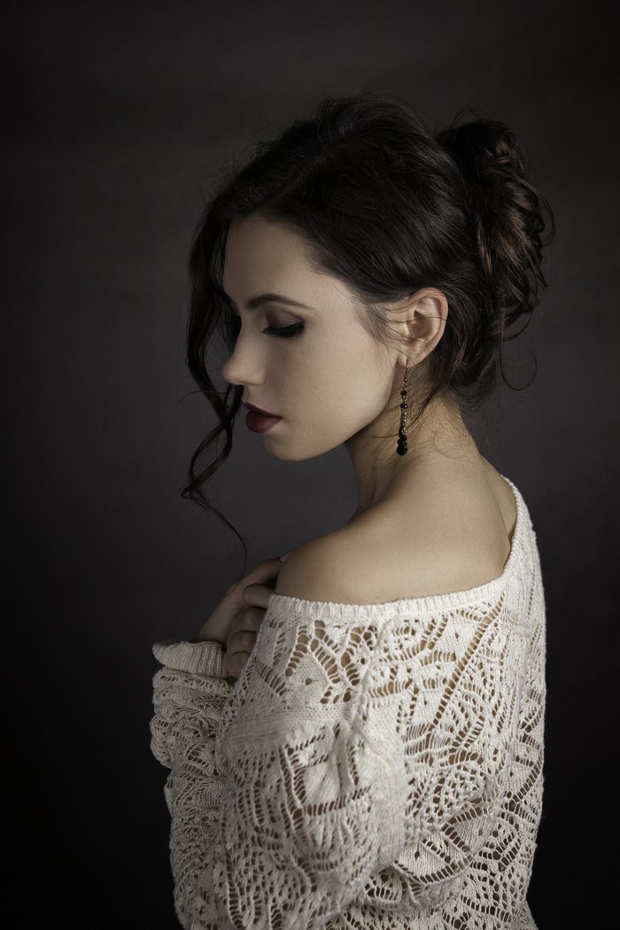 Woman with dark hair in a white lace off-the-shoulder sweater