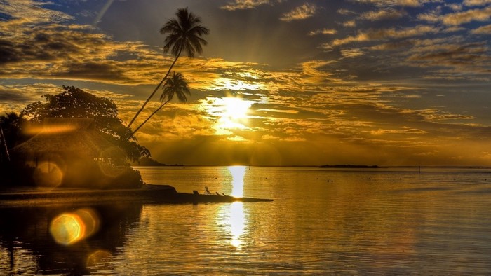 Sunset over the ocean with palm trees and a hut