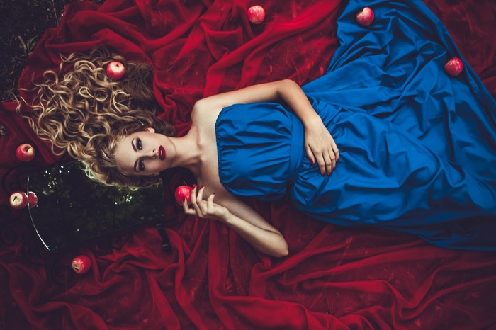 Woman in blue dress with apples on red fabric