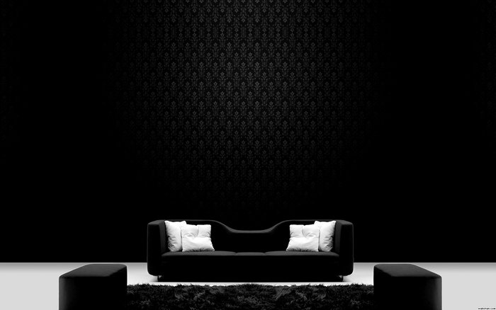 Black couch with white pillows and ottomans on a dark patterned wall