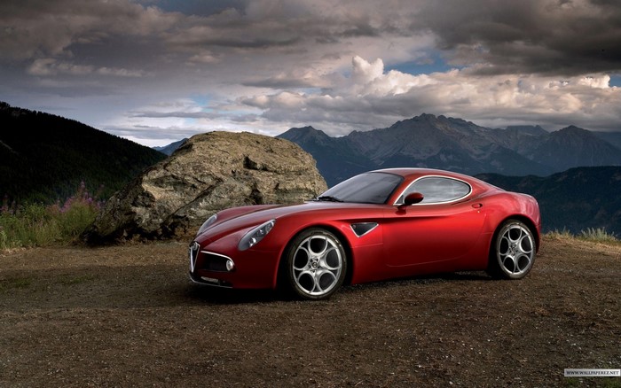 Red Alfa Romeo 8C Competizione parked on a dirt road with mountains