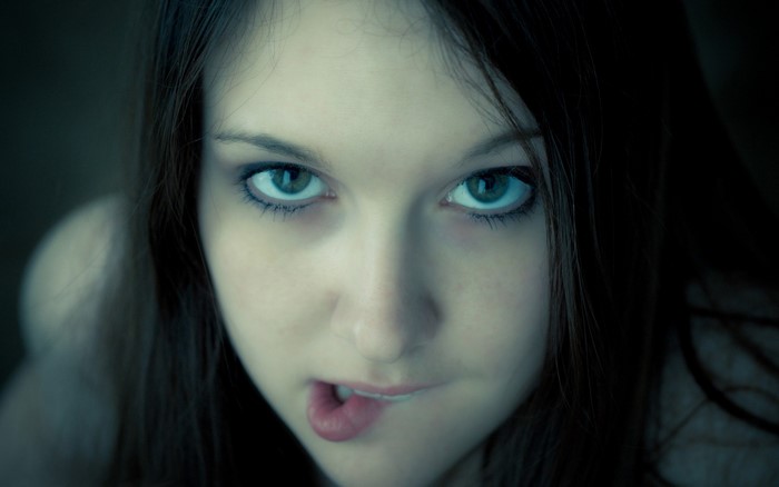Close-up portrait of a young woman with blue eyes biting her lip