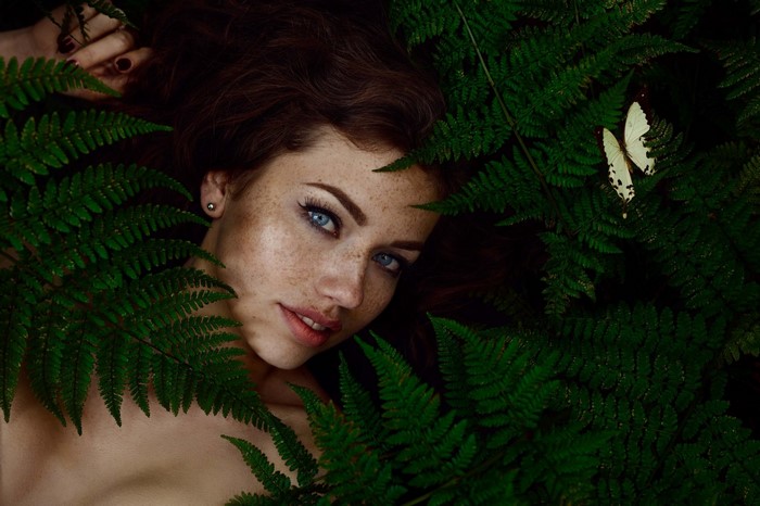 Woman with freckles and blue eyes surrounded by ferns
