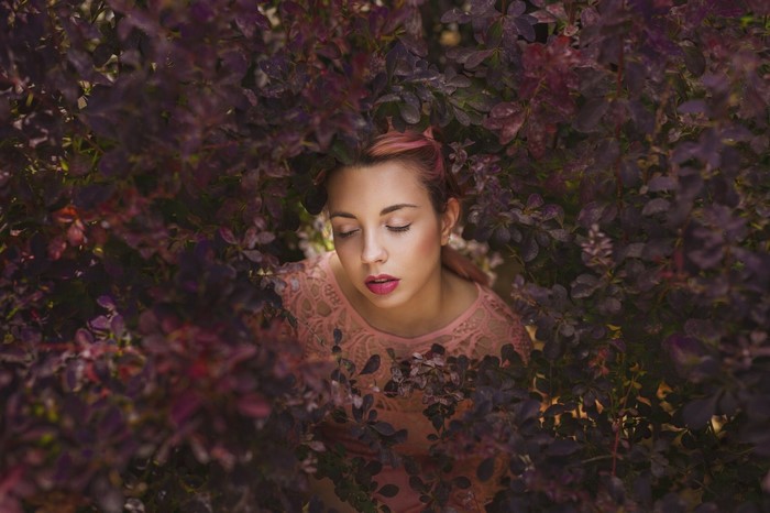 Woman with closed eyes surrounded by purple leaves