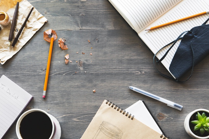 Desk with notebooks, pens, coffee, and plant
