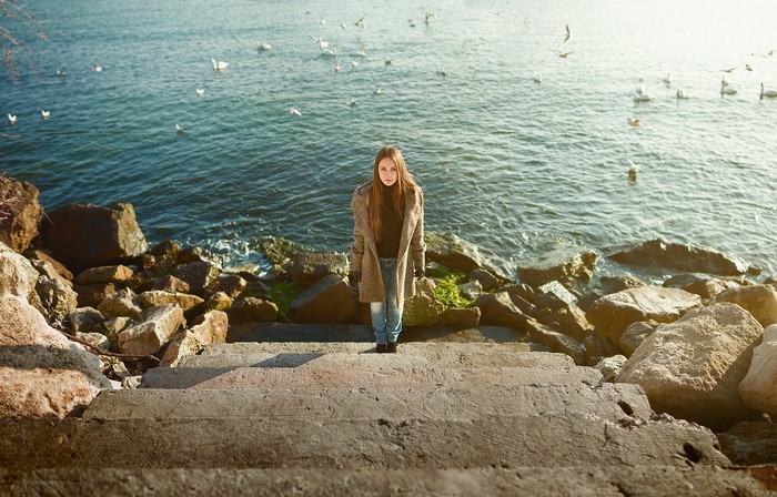 Woman standing on steps by the sea with birds
