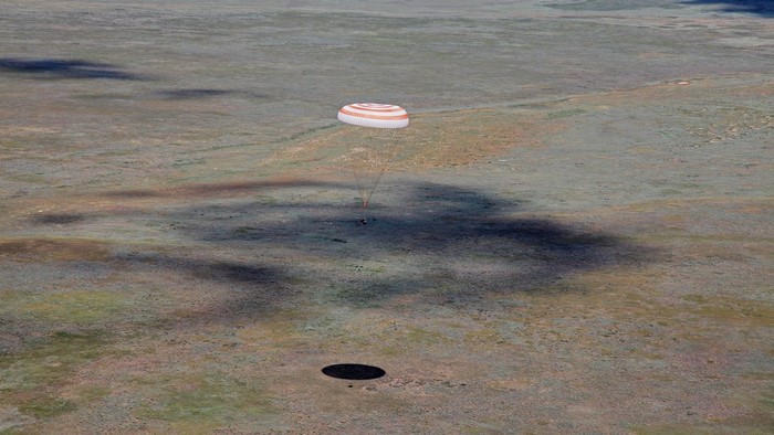 Soyuz capsule landing with parachute over grassy plain