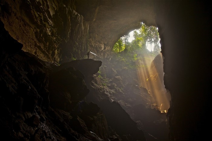 Man with flashlight in a large cave with sunbeams