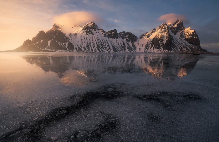 Snow-covered mountains reflecting in icy water at sunset