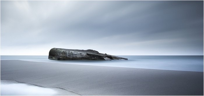 Concrete bunker on a beach with calm sea and overcast sky
