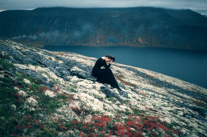 Woman in black dress sitting on a rocky shore overlooking a lake